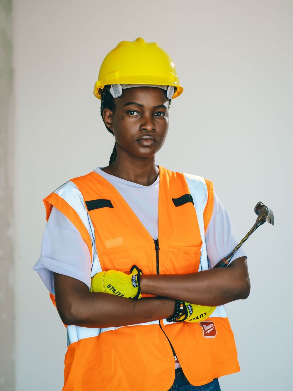 An engineer in an orange vest with arms crossed, holding a hammer