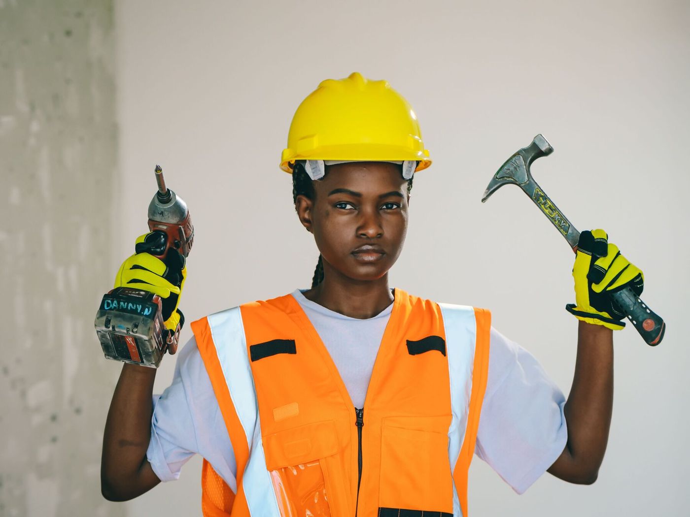 A smiling engineer in a yellow hard hat holding a drill and a hammer