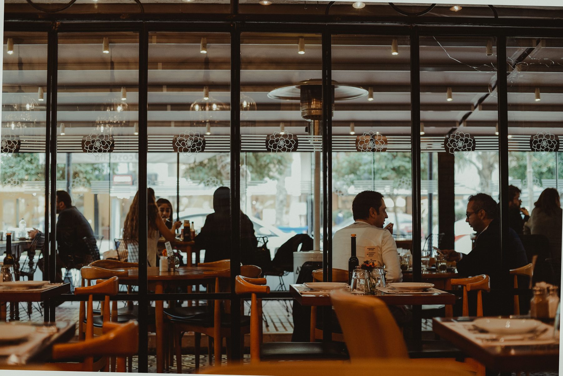A busy dining room with glass walls, wooden chairs and guests at tables