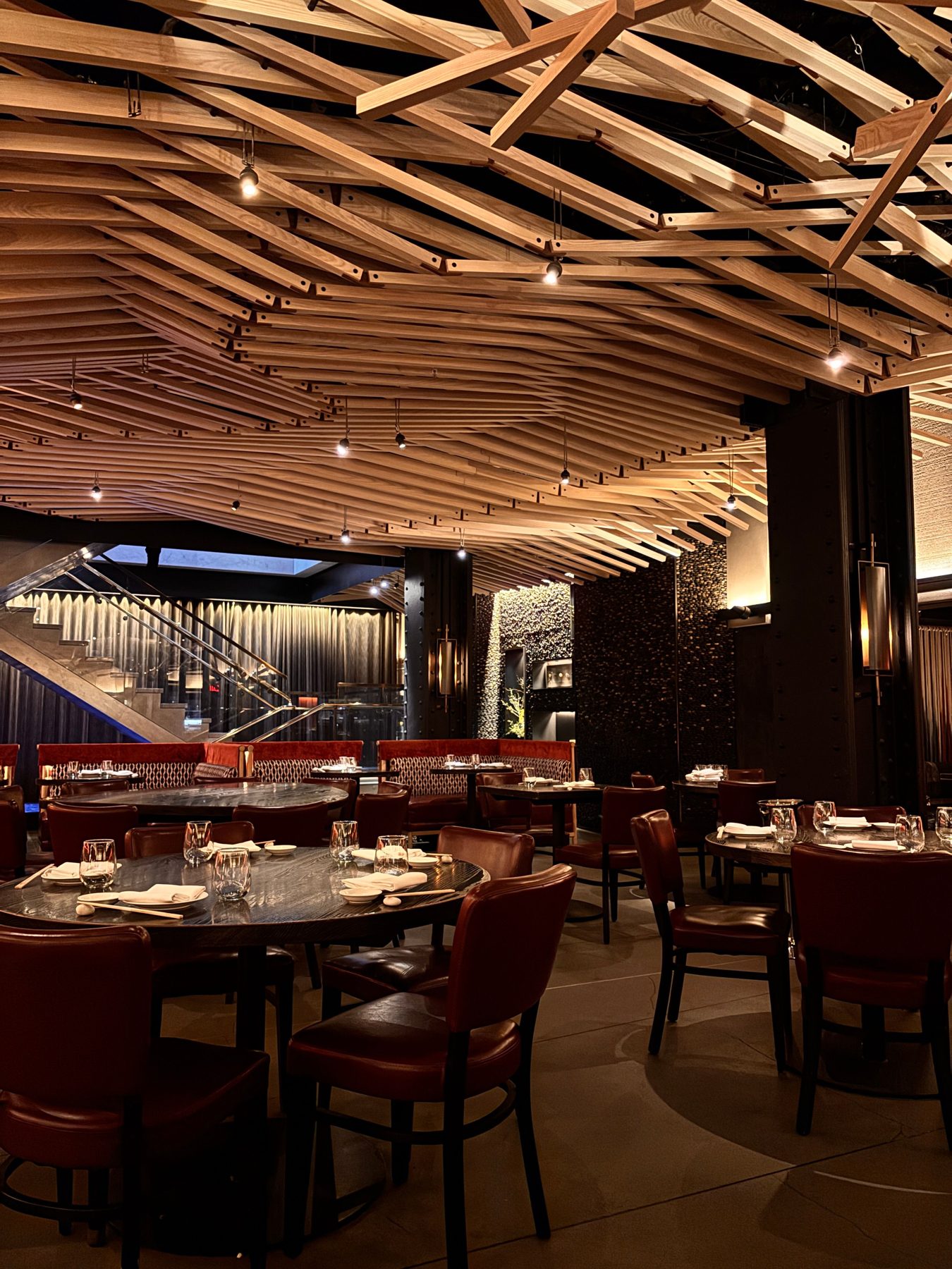 A dining room with a slatted timber ceiling and red chairs around round tables