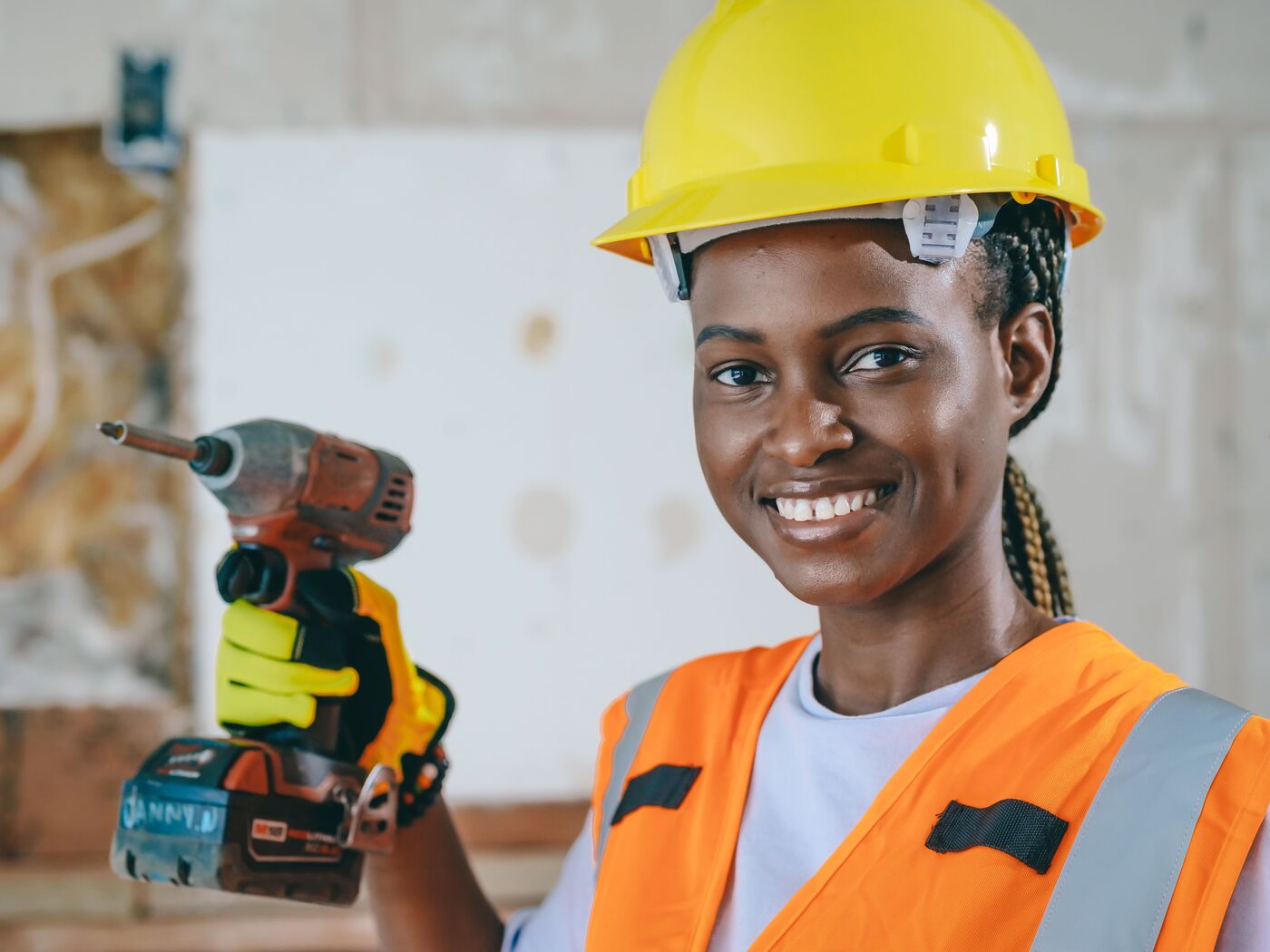 A smiling roofer in a yellow hard hat holding a drill