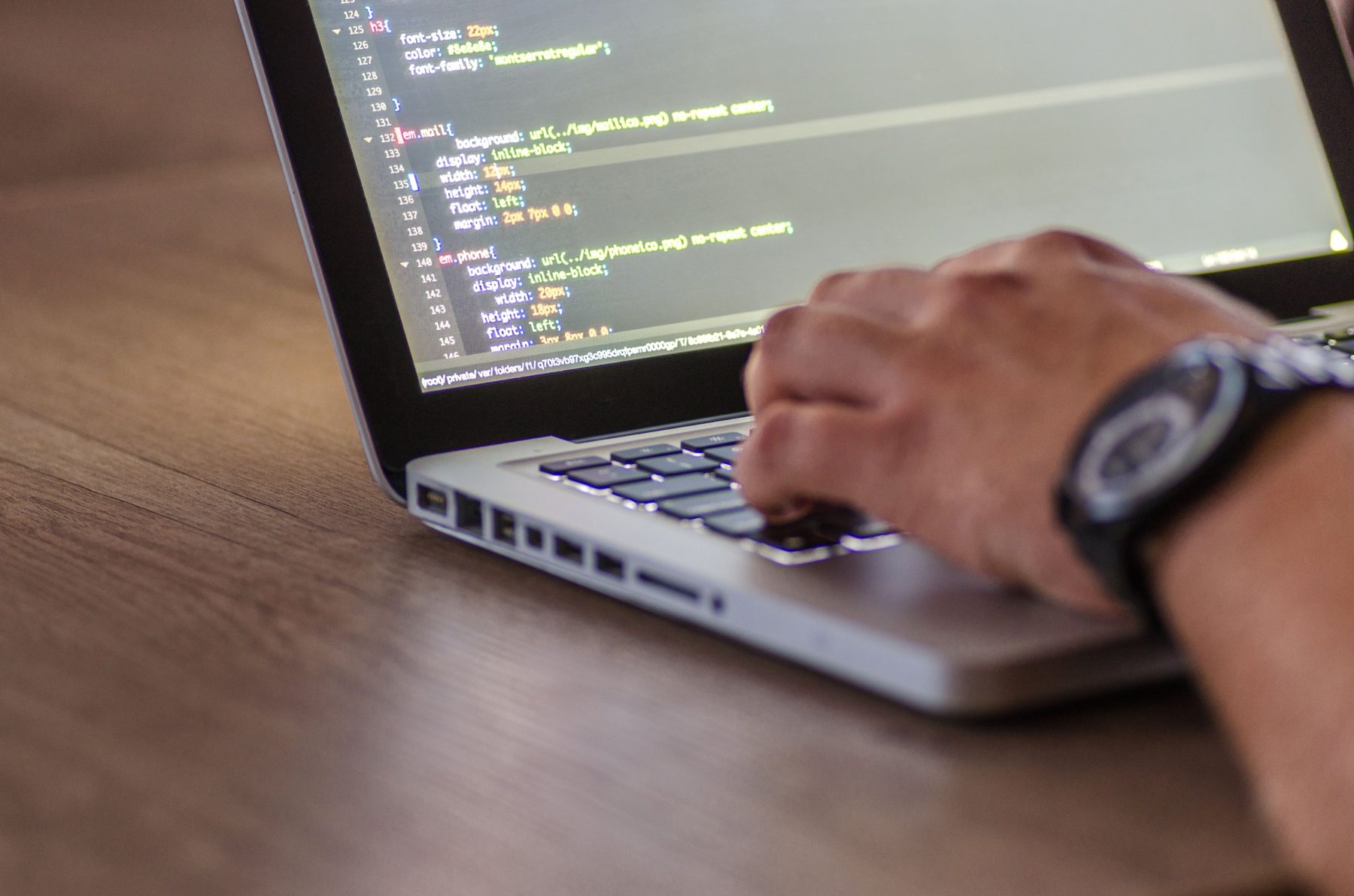 A developer typing on a laptop with code on the screen