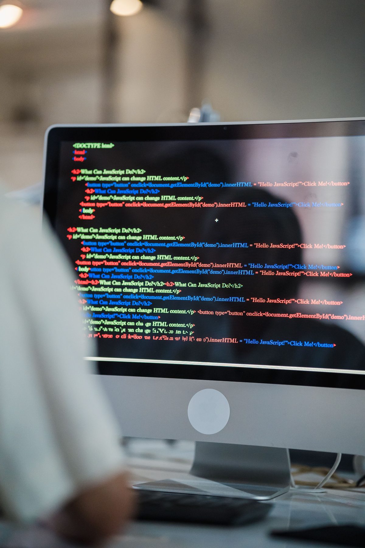 A monitor showing code with a person working beside it
