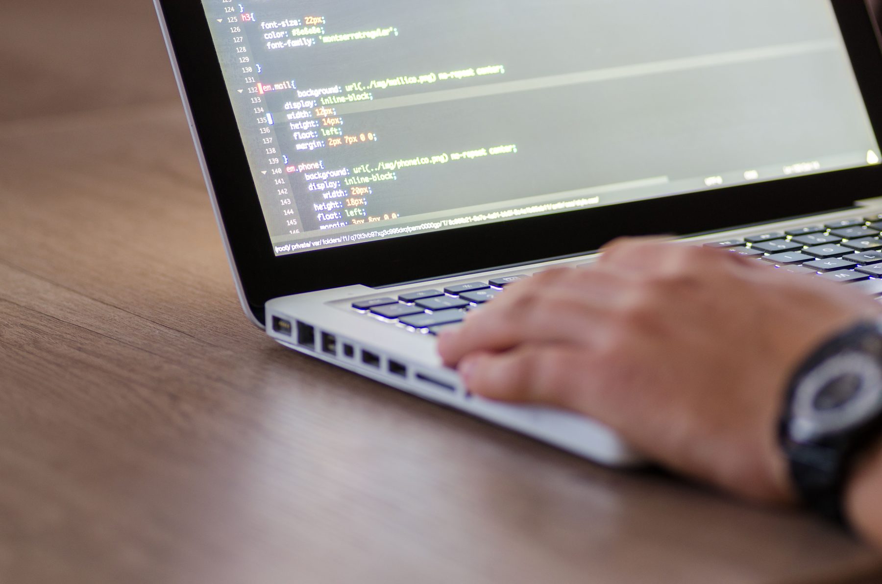 Hands typing on a laptop with code on the screen