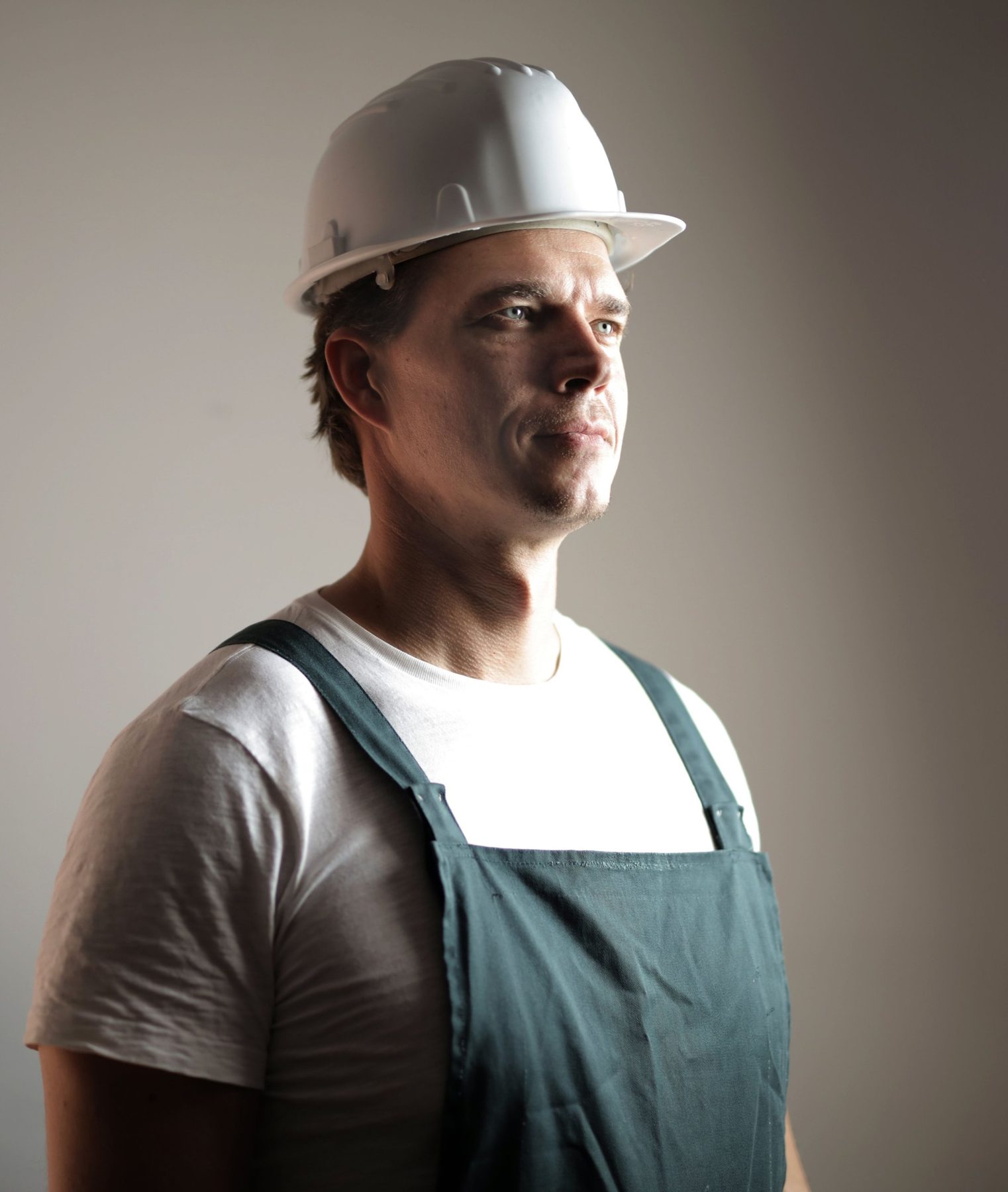 A man in overalls and a white helmet looking off to one side