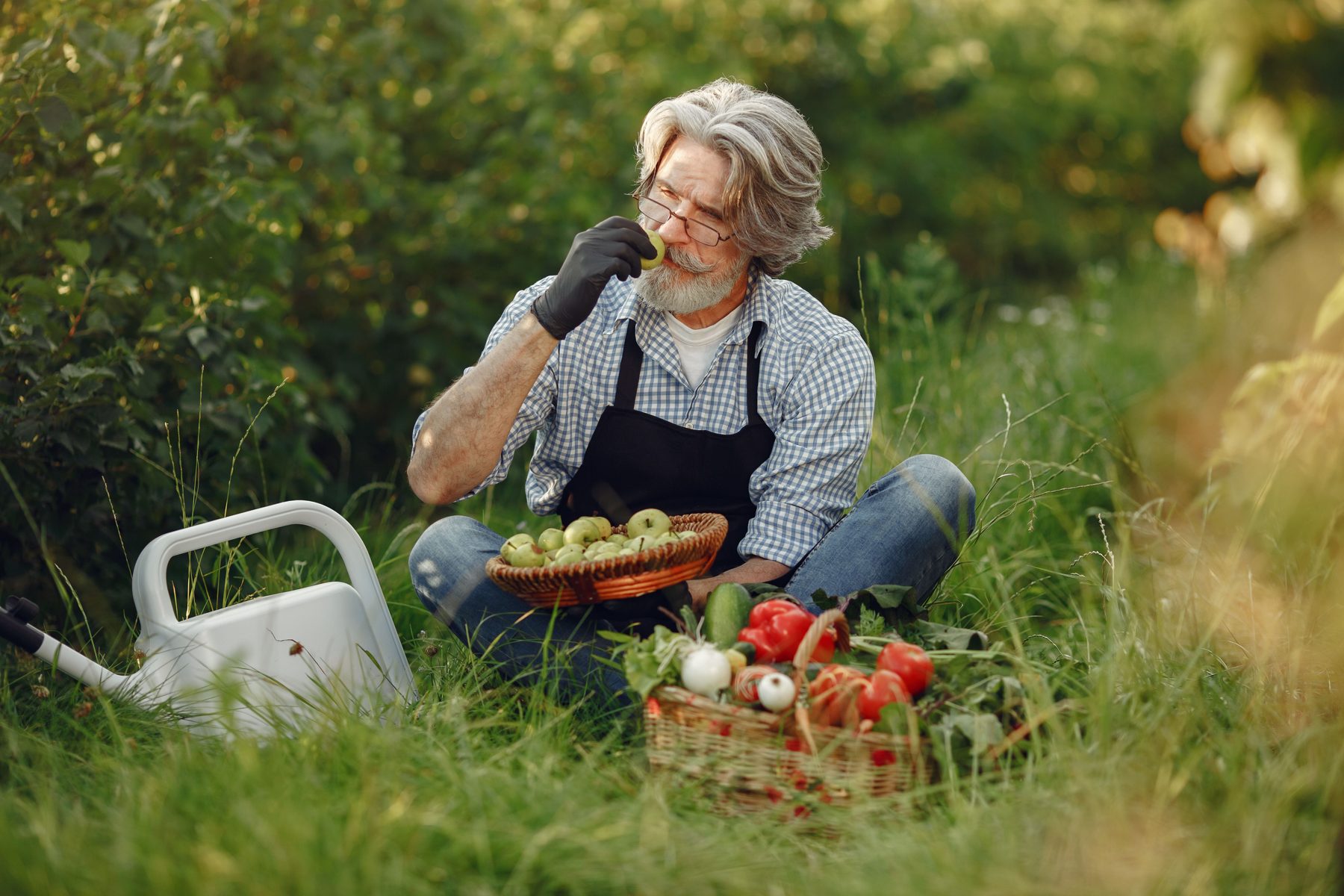 A man resting in long grass beside a watering can and a basket of vegetables