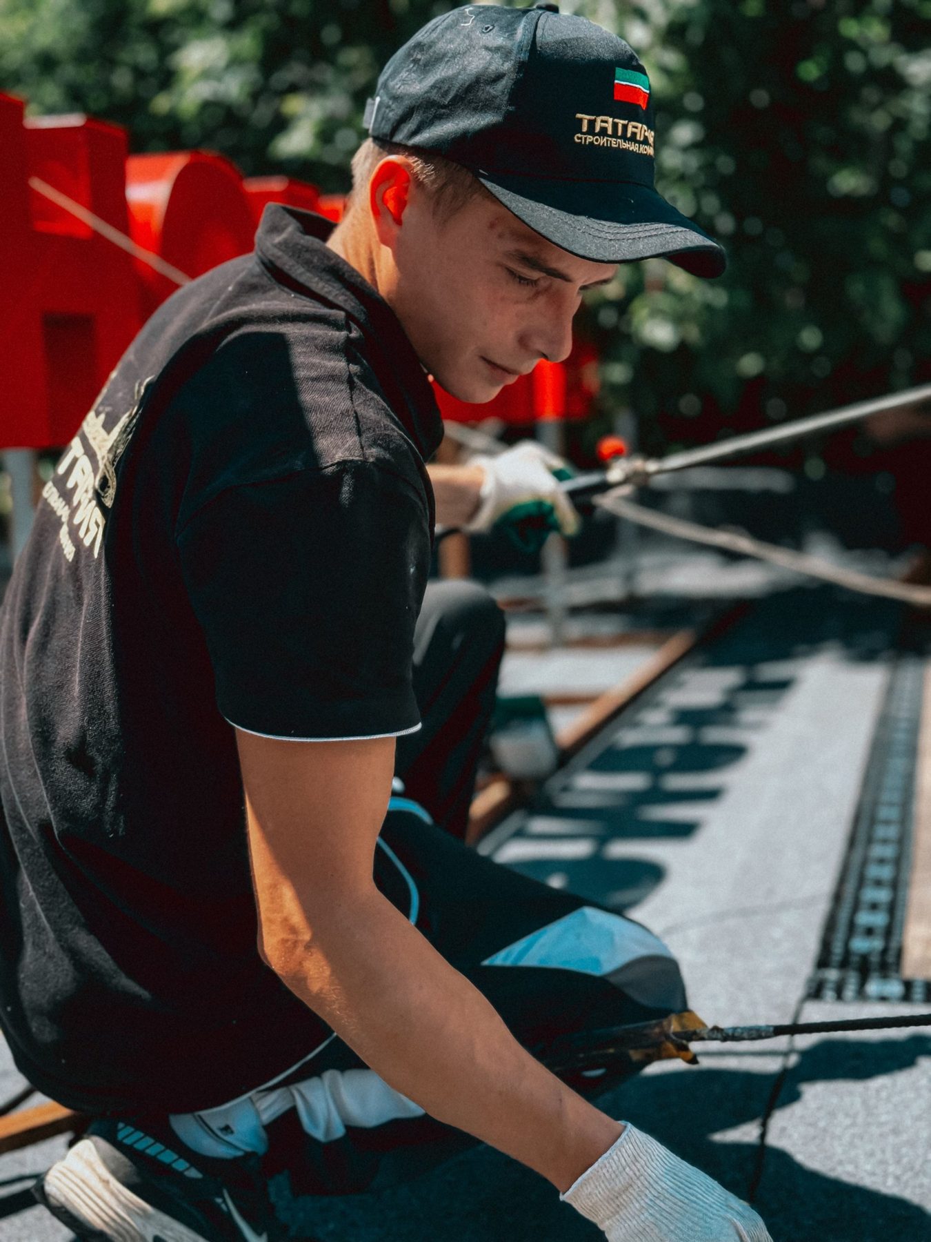 A climber in a cap kneeling on a roof and fixing rope and strapping
